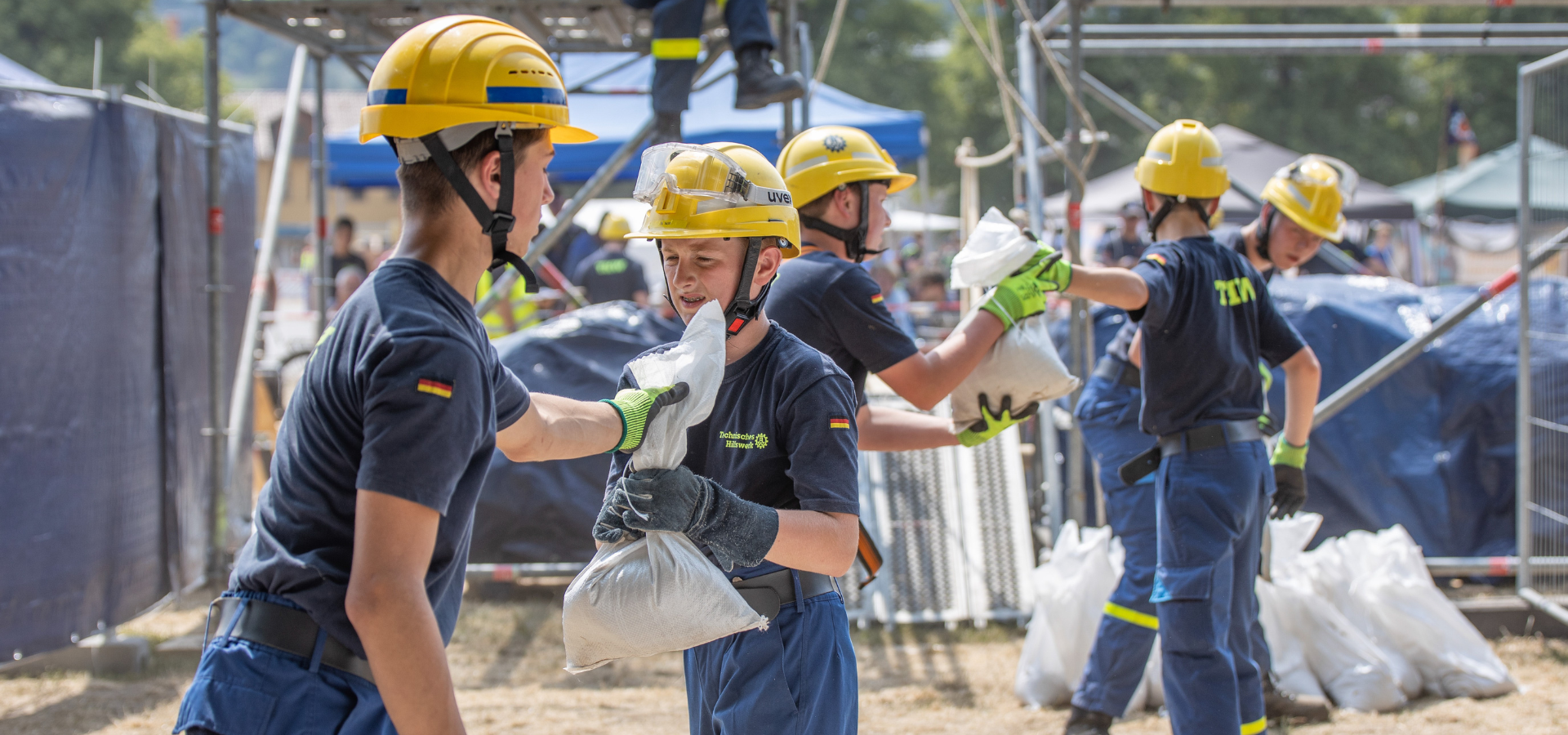 Kinder in Uniform der THW-Jugend reichen sich Sandsäcke entgegen.
